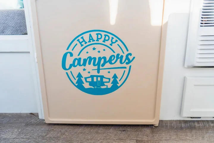 An RV rental's beige mini-fridge boasts a blue "HAPPY Campers" decal, featuring a pop-up camper.. Coleman Grand Tour Sun Ridge 1998