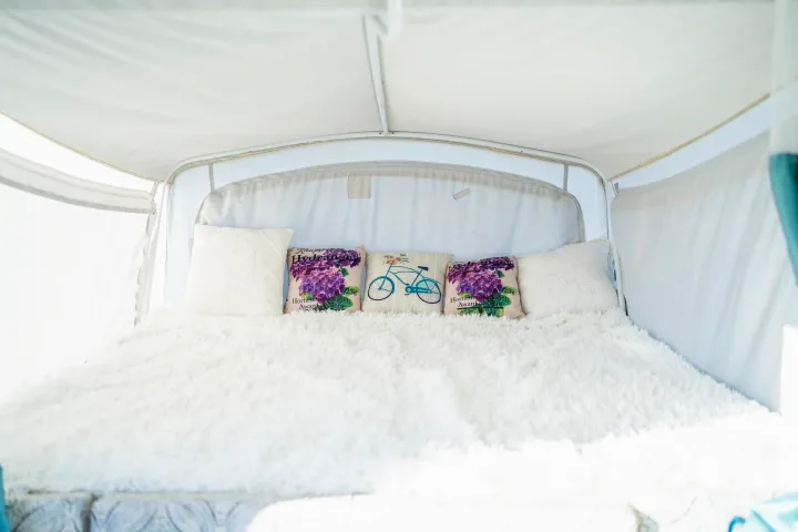 Comfortable bed setup in an RV rental, featuring a white fluffy blanket & decorative pillows with flowers and a bicycle.. Coleman Grand Tour Sun Ridge 1998