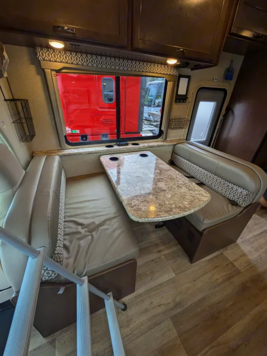 This RV rental's dinette features a U-shaped bench, granite-look table with cup holders, wood-style floor, and large windows.. Thor Freedom Elite 2018