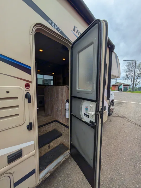 RV rental: View from outside into a beige RV with its door open, revealing interior steps and a fire extinguisher.. Thor Freedom Elite 2018