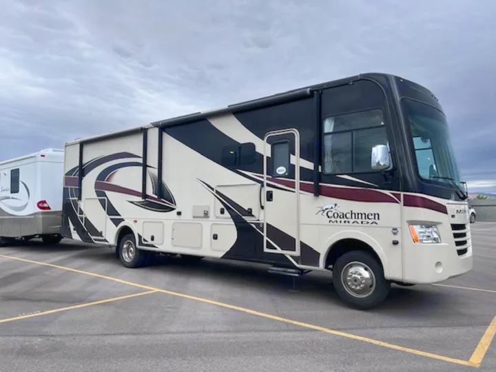 A large Coachmen Mirada motorhome RV rental tows a white travel trailer in a paved parking lot.. Coachmen Mirada 2018
