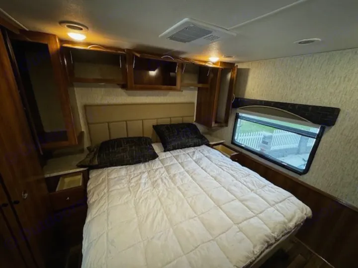 RV rental bedroom featuring a comfortable bed, wood cabinets, and a window with an outdoor view.. Coachmen Mirada 2018
