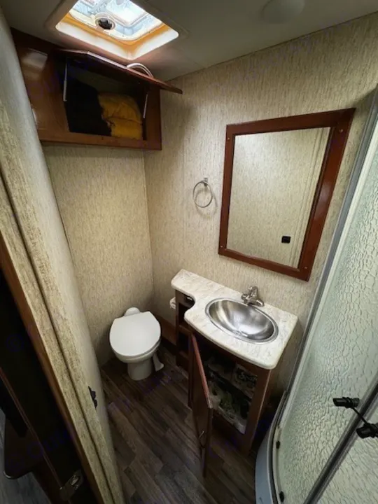 Interior of a compact rv rental bathroom featuring a toilet, sink, mirror, shower, overhead cabinet, and skylight.. Coachmen Mirada 2018
