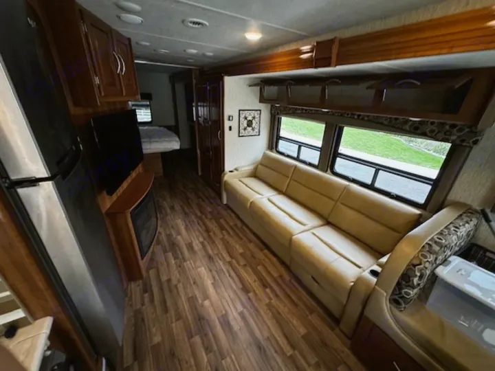 Spacious RV rental interior: comfortable living area with light sofa, TV, fireplace, fridge, and a view into the bedroom.. Coachmen Mirada 2018