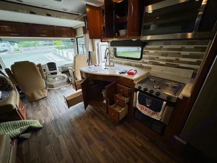 This rv rental's interior boasts a functional kitchen with stove, microwave, open cabinets, and a roomy cockpit area.. Coachmen Mirada 2018