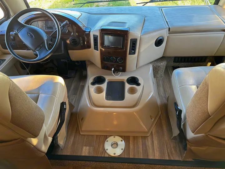 RV rental interior view: spacious driver's cockpit with steering wheel, modern dashboard, infotainment screen, and comfortable seating.. Thor A.C.E. 2017