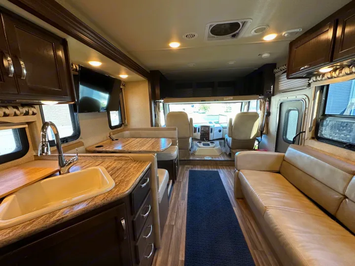 Spacious, modern RV rental interior featuring a full kitchen, dining booth, sofa, and comfortable front cabin seats.. Thor A.C.E. 2017