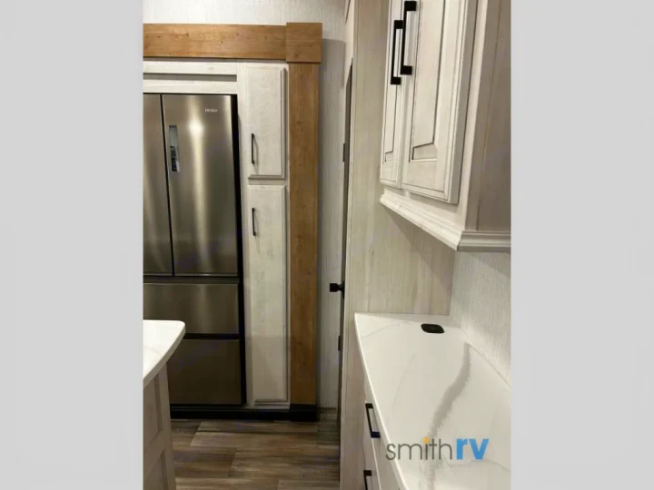 Modern rv rental kitchen featuring a stainless fridge, light cabinets, and a sleek marble-patterned counter.. Heartland Bighorn 2023
