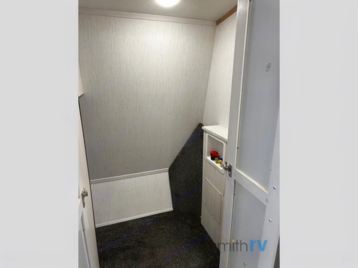 Inside an RV rental: a compact utility closet with visible plumbing/electrical connections and dark carpeted floor.. Heartland Bighorn 2023