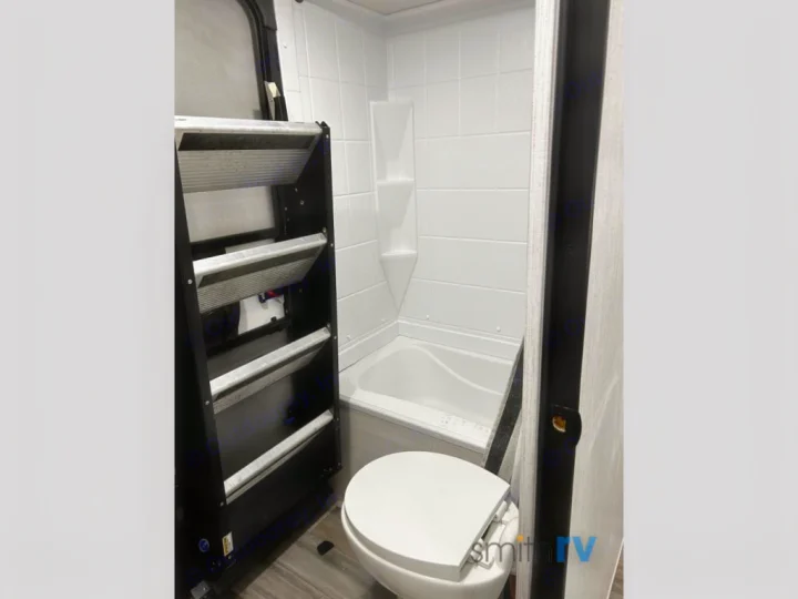 Compact rv rental bathroom with toilet, small tub/shower, and black bunk bed ladder on the left.. Heartland Bighorn 2023