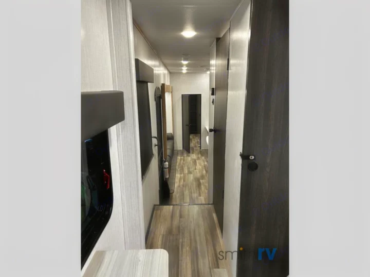 Inside a modern RV rental: View down a clean hallway with light walls, dark doors, and wood-look flooring.. Heartland Bighorn 2023