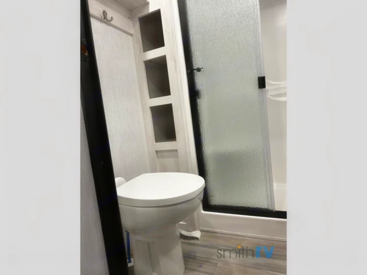 Clean RV rental bathroom: features a toilet, textured glass shower, and built-in storage shelves.. Heartland Bighorn 2023