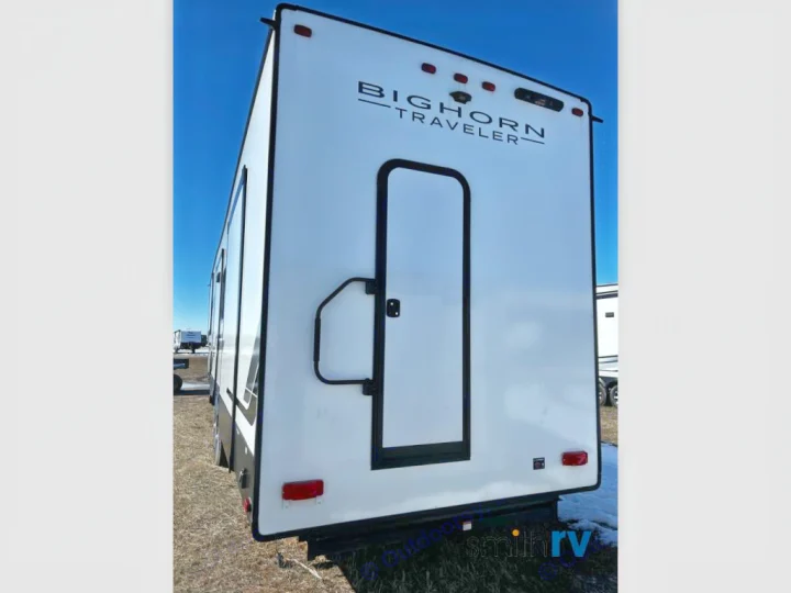 Rear of a white Bighorn Traveler RV, ideal for an rv rental. Visible door, lights & "BIGHORN TRAVELER" text.. Heartland Bighorn 2023