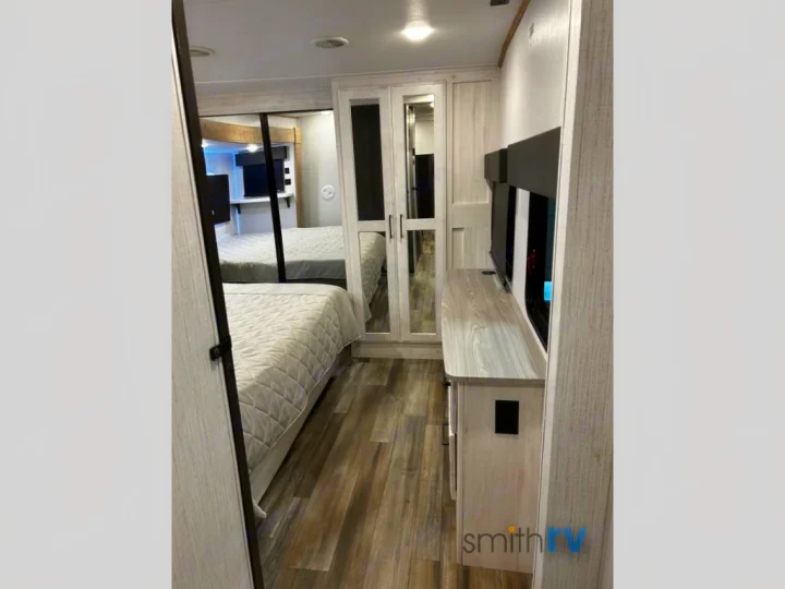 This modern RV rental bedroom/walkway showcases a cozy bed, mirrored closet reflecting the space, and media console. Ideal for travel.. Heartland Bighorn 2023