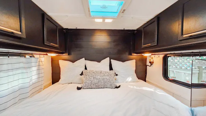 Cozy RV rental bedroom interior. Features a large white bed, dark wood headboard, overhead cabinets, and skylight.. Terry Fleetwood 1991