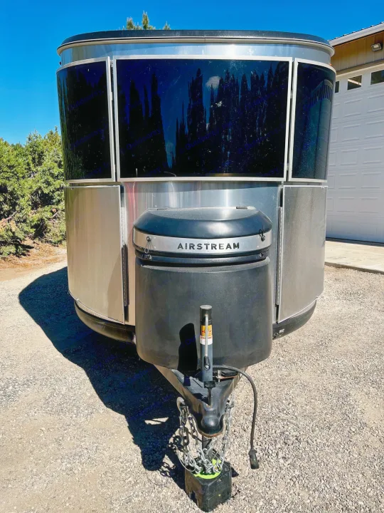 Sleek silver Airstream travel trailer's front, with 'AIRSTREAM' logo, parked on gravel. Perfect for your next RV rental adventure!. Airstream Base Camp 2021