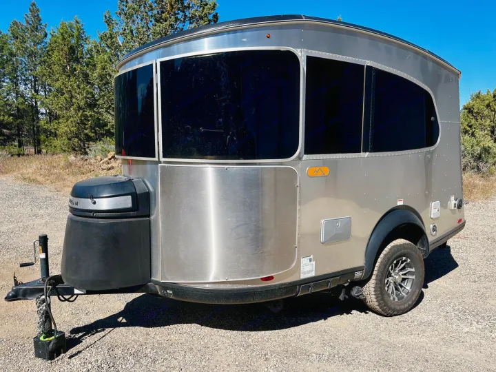 A modern, silver travel trailer, ideal for an RV rental. Parked outdoors on gravel, ready for your next adventure.. Airstream Base Camp 2021