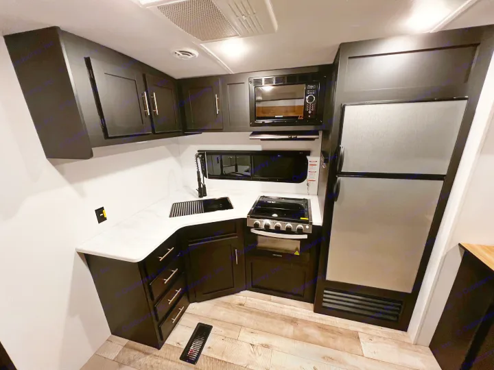 Modern RV rental kitchen interior: dark cabinets, light countertops, sink, stovetop, oven, microwave, and refrigerator.. Keystone RV Springdale 2022
