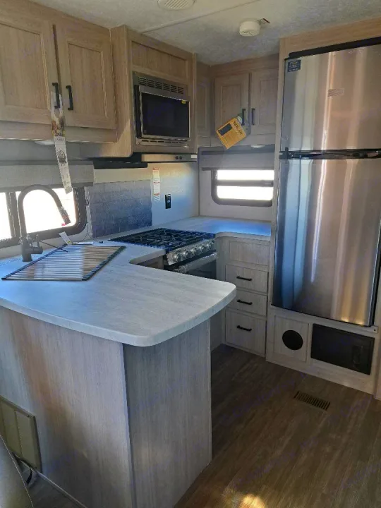 Bright RV kitchen: stainless steel fridge, microwave, stove, sink, and light wood cabinets. Great for rv rental.. Forest River Aurora Aurora 2024