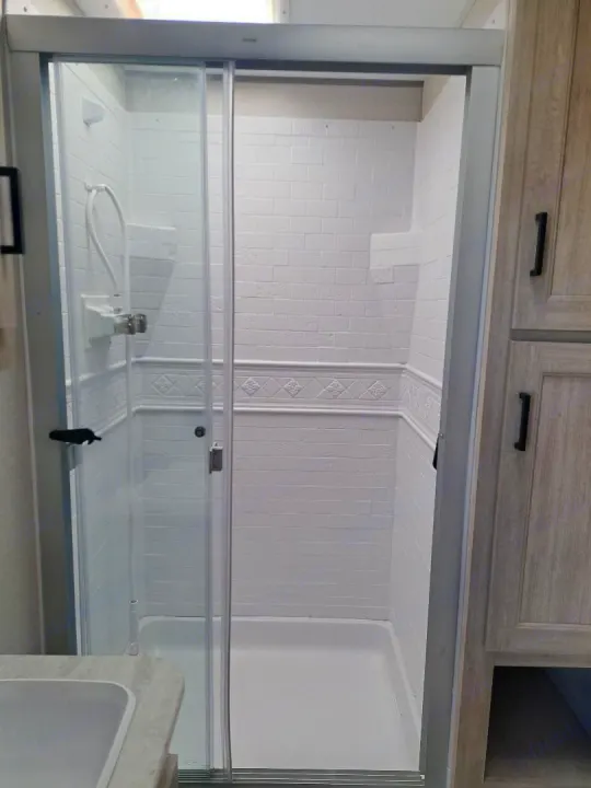RV rental: Clean, compact shower with white faux brick walls, decorative border, and a sliding glass door for travel comfort.. Forest River Aurora Aurora 2024