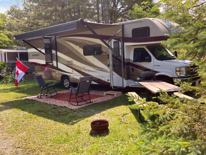 Class C RV rental at a sunny campsite with extended awning, outdoor seating, picnic table, and fire pit.. Forest River Sunseeker 2018