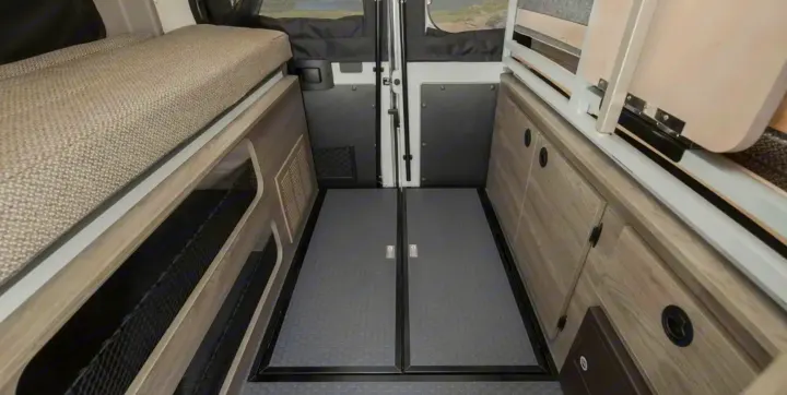 Compact RV rental interior featuring a bed, ample storage cabinets, and durable textured flooring. Ideal for road trips.. Winnebago Solis 2021