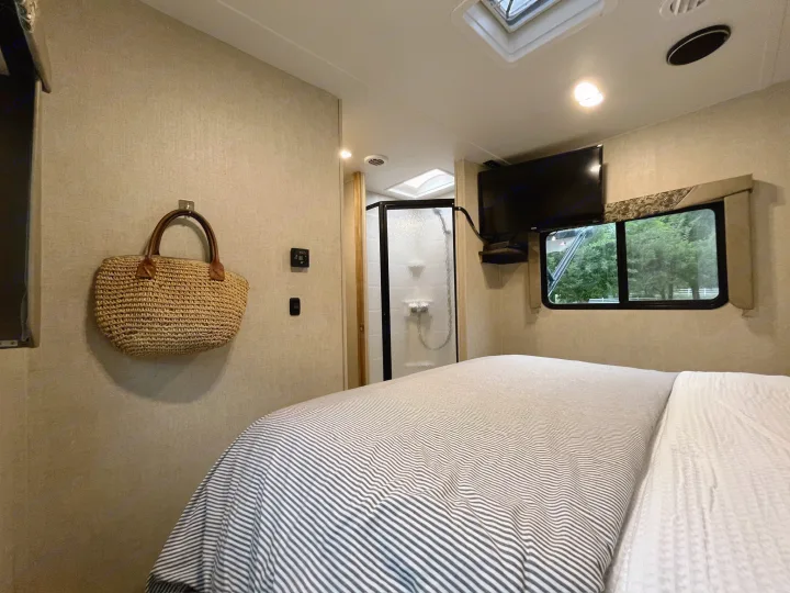 Cozy RV rental bedroom featuring a striped bed, wall-mounted TV, window view of nature, and an ensuite shower.. Gulf Stream Conquest 2017