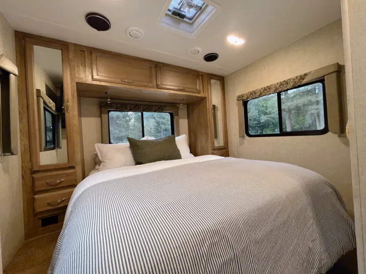 Cozy RV rental bedroom interior featuring a comfortable bed, ample wood cabinetry, and windows overlooking scenic trees.. Gulf Stream Conquest 2017