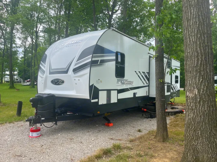 White Fuzion Impact Edition travel trailer, an RV rental, set up at a shaded campground for camping.. Keystone RV Fuzion Impact Toy Hauler 2022