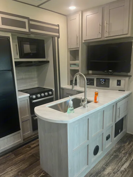 Spacious RV rental interior featuring a modern kitchen with island sink, stove, fridge, TV, and light cabinets.. Keystone RV Fuzion Impact Toy Hauler 2022
