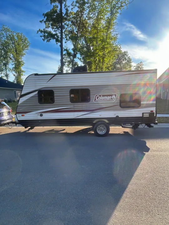 A white and brown Coleman travel trailer is parked on an asphalt road, ready for rv rental adventures.. Coleman Lantern 17FQ 2020