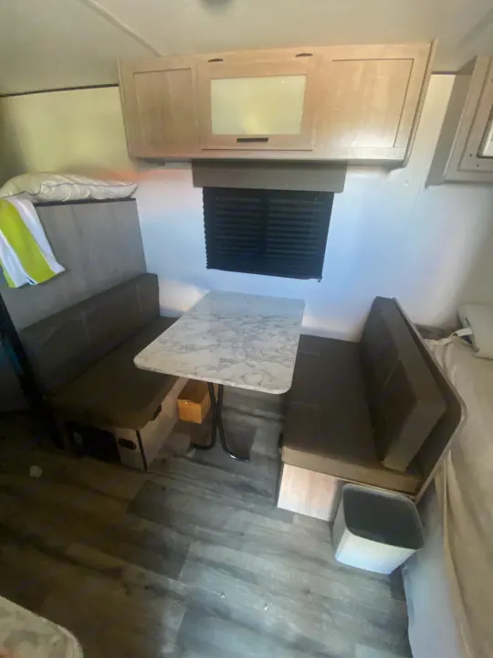 **RV rental** dinette area featuring a marble-look table, two upholstered benches, and overhead cabinets. Ideal for **camper** meals.. Coleman Lantern LT 17b 2024