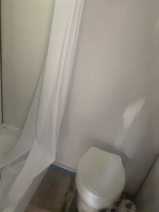View inside an RV rental bathroom, featuring a white shower curtain on the left and a compact toilet on the right.. Coleman Lantern LT 17b 2024