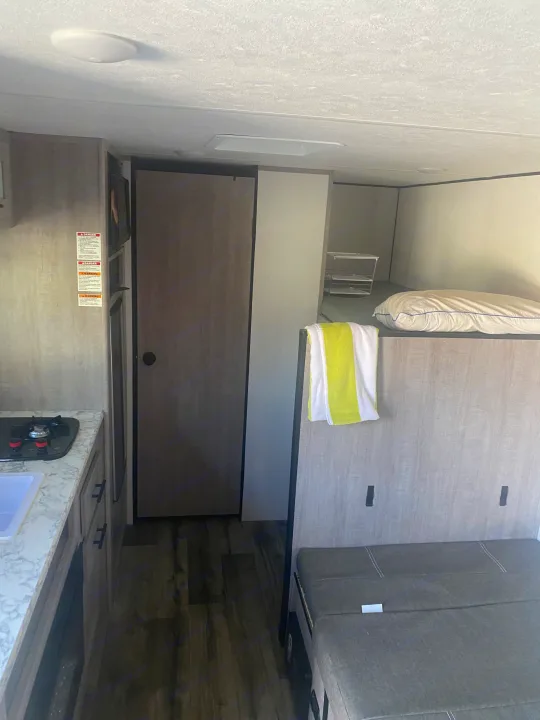 Compact RV rental interior featuring a kitchenette, bunk beds, and a versatile seating/sleeping area.. Coleman Lantern LT 17b 2024