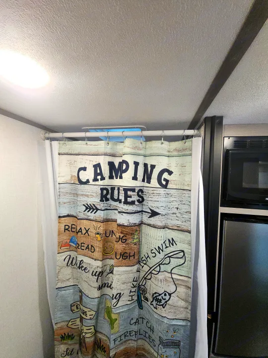 Inside an RV rental: a "Camping Rules" shower curtain provides fun decor, with a microwave and refrigerator visible in the compact interior.. Colemen Dutchmen 17R 2024