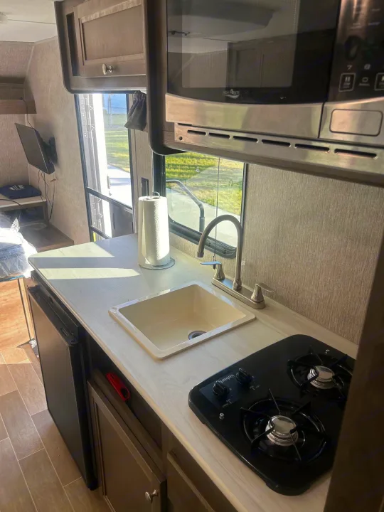 Compact RV rental kitchen with sink, microwave, 2-burner stove, fridge, & wall-mounted TV for on-the-go living.. Coleman Lantern 17FQ 2020