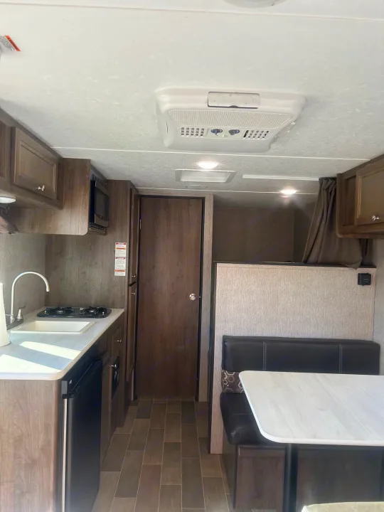 RV rental interior: compact kitchen with sink, stove, microwave; dinette; and a private sleeping area.. Coleman Lantern 17FQ 2020