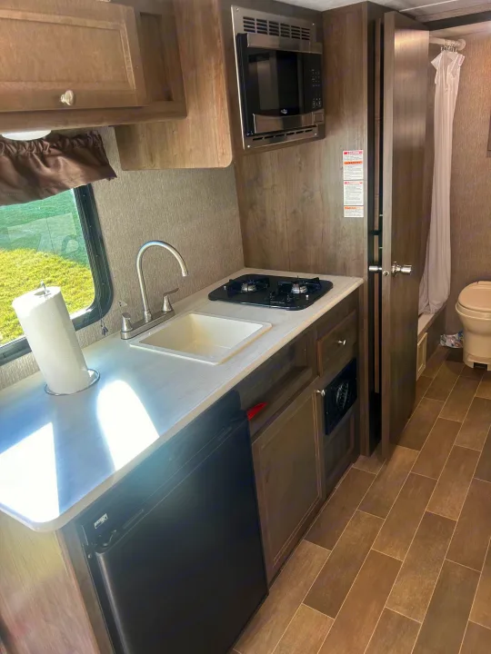 RV rental: Compact interior with kitchen (sink, stove, microwave, fridge) and a small bathroom. Light streams from a window.. Coleman Lantern 17FQ 2020