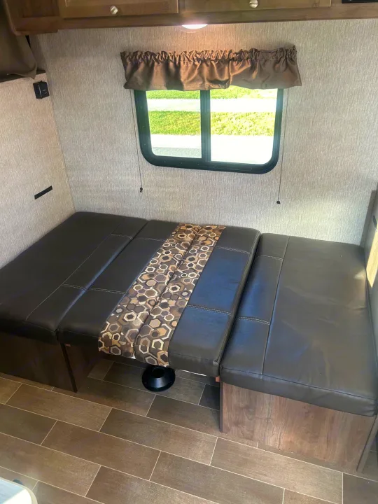 Inside this RV rental, a brown faux-leather dinette easily converts to a bed, offering comfort for your adventures.. Coleman Lantern 17FQ 2020