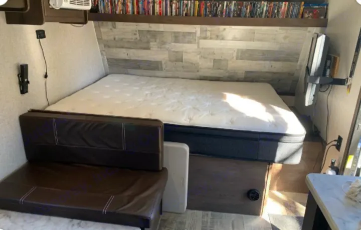 This RV rental offers a compact bedroom/living area with a large bed, seating, entertainment shelf, and wall-mounted TV.. Dutchmen Coleman Lantern 2021