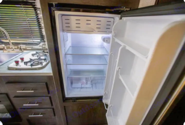 Inside an RV rental: a well-equipped compact kitchen with an open fridge, two-burner stove, and sink.. Dutchmen Coleman Lantern 2021
