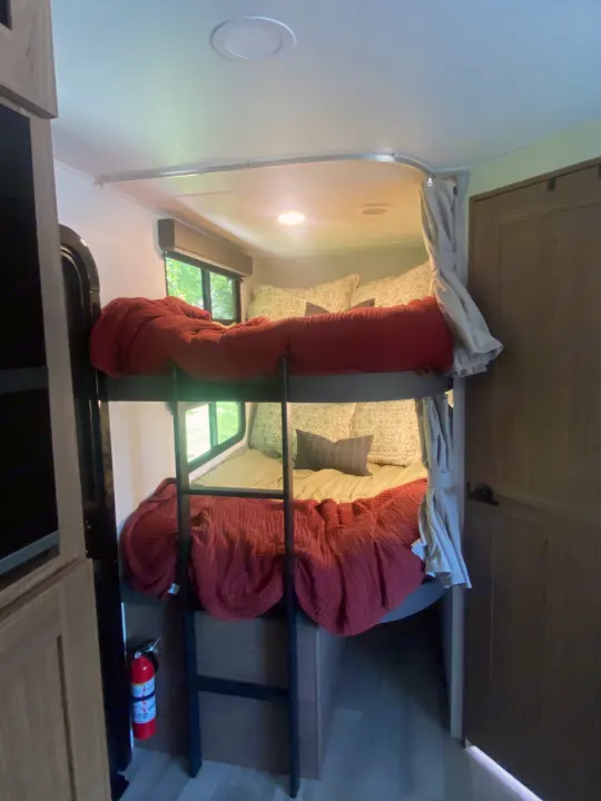 RV rental interior shows bunk beds with red comforters, curtains, windows, ladder, and a fire extinguisher.. Alliance Delta 251BH 2024