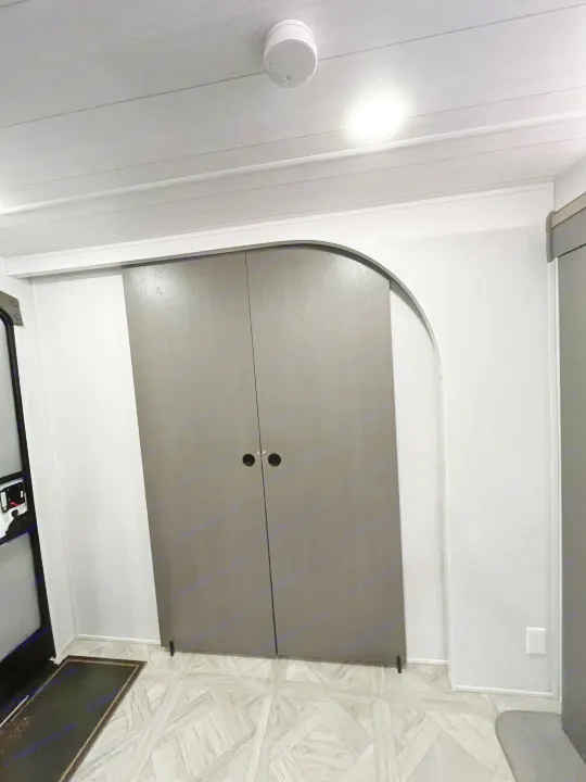 RV rental interior: modern closet with arched top, textured walls, and geometric floor. Functional space includes a smoke detector & light.. Forest River Wildwood Platinum 2024