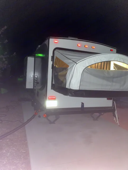 Night shot of an **RV rental**: a hybrid **travel trailer** with a tent bunk end extended & lights on, set up for **camping**.. Jayco Jay Feather 7 2016