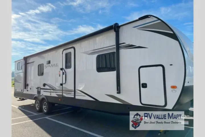 Modern white Solaire travel trailer, ideal for an RV rental. This spacious RV features windows, a side door, and an awning, parked outdoors.. Forest River Palomino Solaire 2023