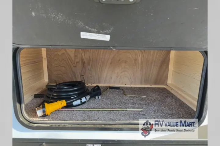 RV rental's open storage compartment, with a coiled power cord, yellow electrical adapter, and crank on a carpeted floor.. Forest River Palomino Solaire 2023