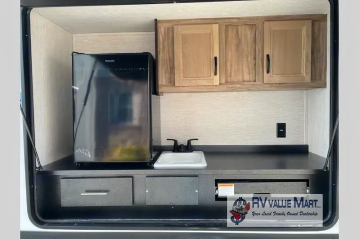 Explore this RV rental's convenient outdoor kitchen featuring a mini-fridge, sink, and ample storage, ideal for camping adventures.. Forest River Palomino Solaire 2023