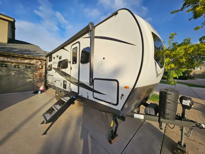 White MicroLite travel trailer RV rental, with steps down, parked in a sunny driveway next to a house.. Forest River Flagstaff Micro Lite 2023