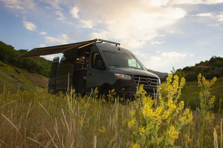 Adventure awaits! Dark gray Sprinter RV rental with awning extended, parked in a field of yellow flowers.. Mercedes-Benz Sprinter 4x4 2022