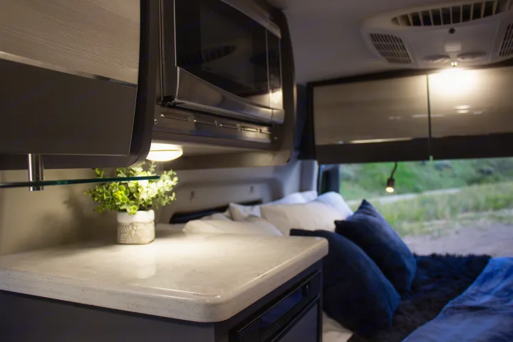 Cozy RV rental interior: modern kitchenette with microwave, counter, potted plant, and comfortable bed area with an outdoor view.. Mercedes-Benz Sprinter 4x4 2022
